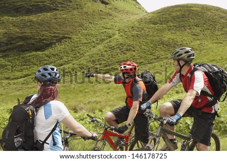 Three cyclists with bikes on lush landscape