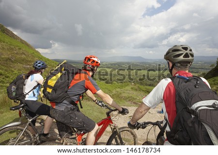 Three cyclists with bikes on track looking at landscape