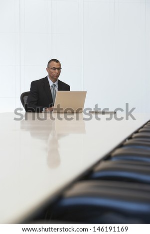 Serious middle aged businessman using laptop in board room