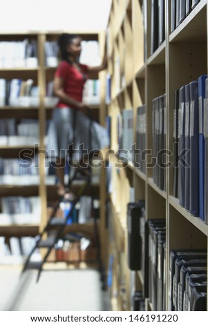 Side view of a blurred female office worker standing on ladder in file storage room