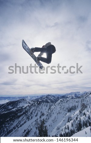 View of a person on snowboard jumping midair over snowed mountains