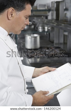 Side view of a middle aged male chef reading recipe book in the kitchen