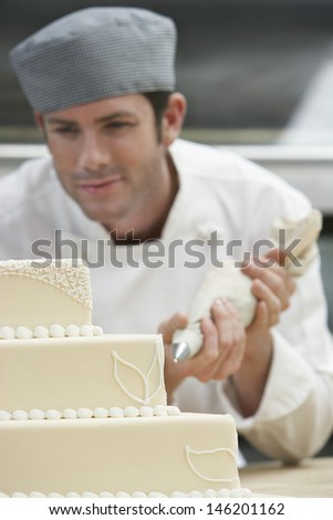 Male chef icing wedding cake in kitchen