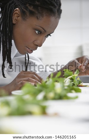 Closeup side view of a female chef preparing salad in kitchen