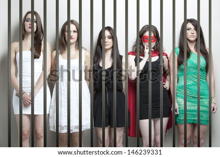 Woman in superhero costume with female friends standing behinds prison bars