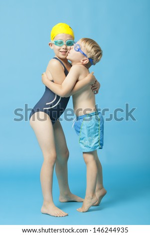 Young siblings in swimwear embracing and kissing over blue background