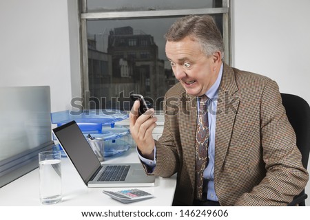 Angry middle-aged businessman looking at cell phone in office