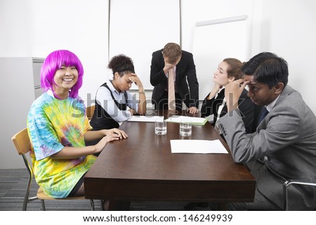 Tired multiethnic businesspeople with colleague in pink wig at meeting