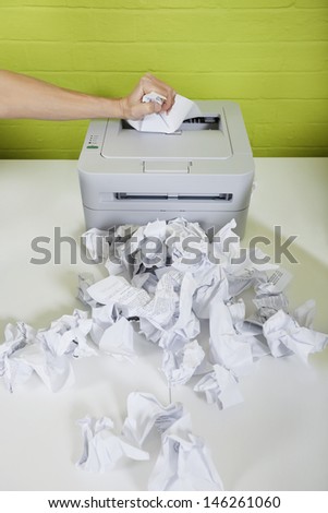 Cropped image of businessman\'s hand using printer with paper balls on desk
