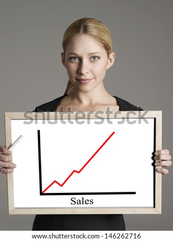 Portrait of young businesswoman showing sales graph against gray background