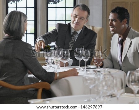 Three businesspeople sitting at restaurant table as man pours wine