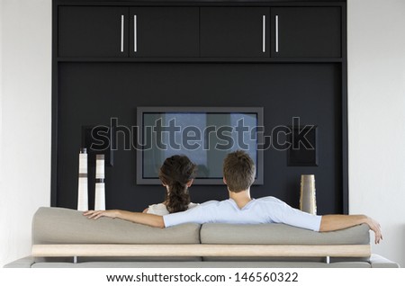 Rear view of young couple watching TV together in living room