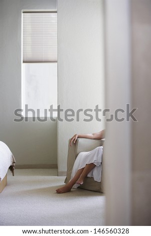 Low section of woman relaxing on armchair in bedroom