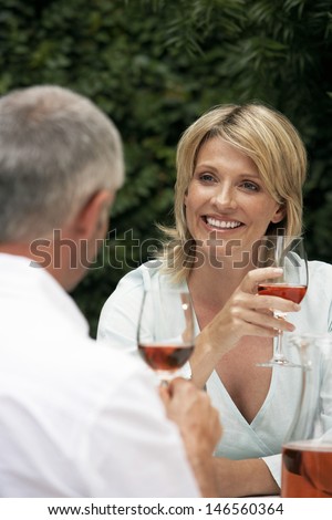 Happy woman looking at man while having red wine at lawn