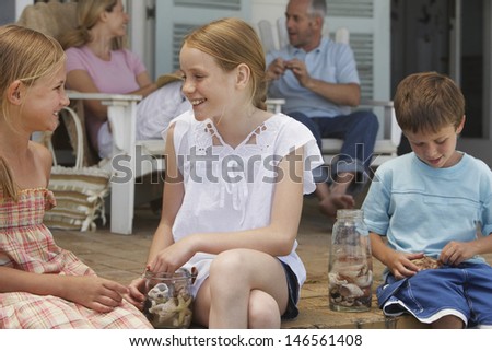 Happy children playing with seashells while sitting at porch with parents in background