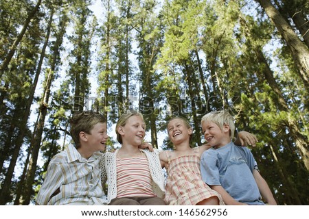 Low angle view of happy young boys and girls sitting arm around in forest