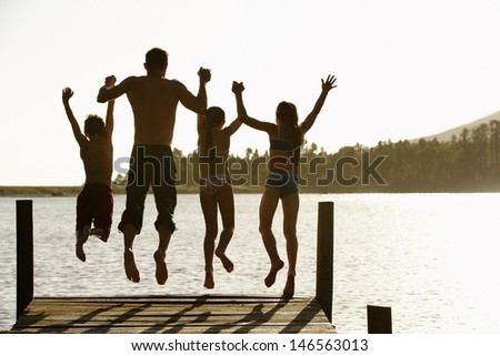 Rear view of father with children holding hands while jumping off a jetty