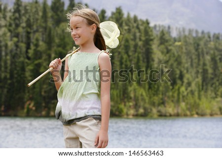 Happy young girl with butterfly net standing by lake