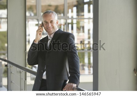 Happy middle aged businessman using cell phone in office