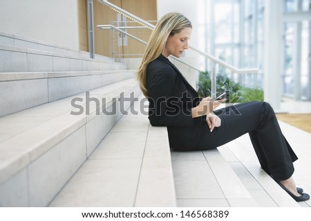Full length side view of young businesswoman reading text message on office steps