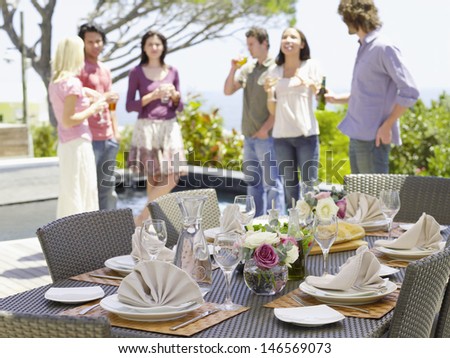Fine dining table setting with friends enjoying drinks in background