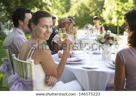 Portrait of beautiful bride holding champagne flute while sitting with guests at wedding table
