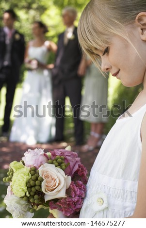 Cute little flower girl holding bouquet with guests and wedding couple in background