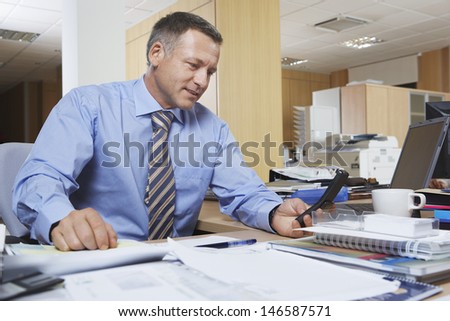Middle aged businessman using cell phone at office desk