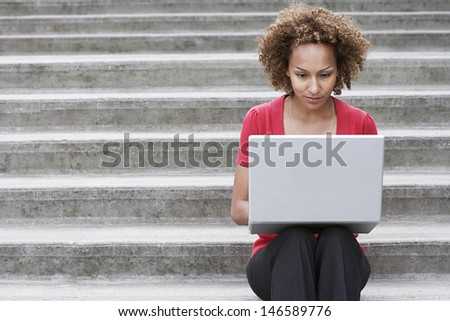 Young African American woman using laptop on steps outdoors