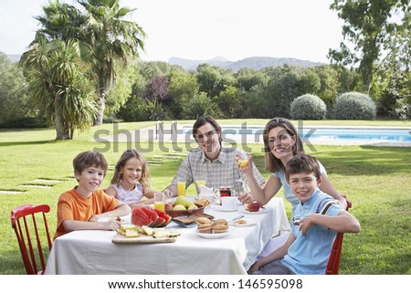 Portrait of a smiling couple with three children sitting at breakfast table in the garden