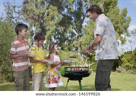 Side view of father serving grilled food to children in the garden