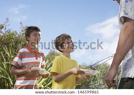 Cropped father serving grilled frankfurters to sons in the garden