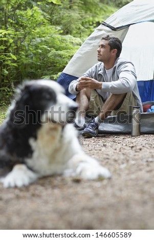 Young man looking away by tent with blurred dog in foreground