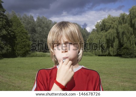 Closeup portrait of a little boy blowing whistle in meadow