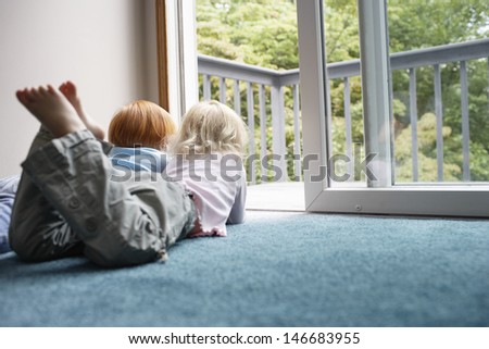 Young sisters looking out through balcony while lying on carpet at home
