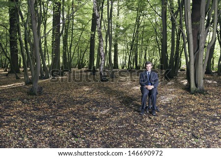 Full length portrait of businessman sitting in middle of forest