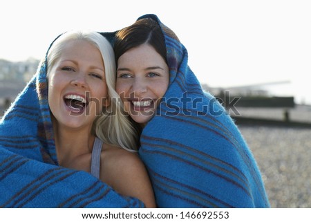 Portrait of cheerful young women wrapped in blanket laughing at beach