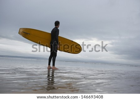 Full length of young male surfer with surfboard looking at sea on beach