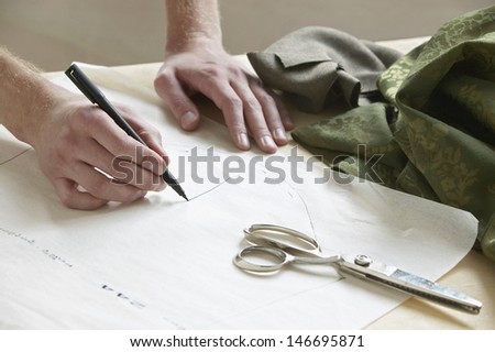 Cropped image of male tailor drawing pattern on paper at table