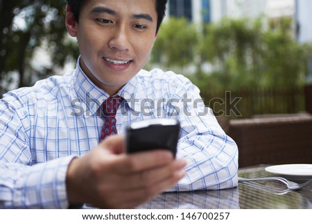 Closeup of young businessman using cell phone at outdoor cafe
