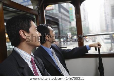 Side view of two businessmen sitting in double decker tram