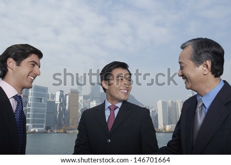 Three multiethnic business people discussing with city skyline in background