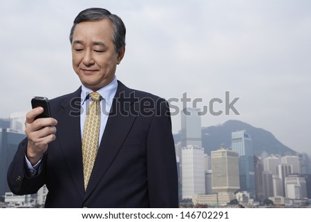 Middle aged businessman reading text message on cell phone with cityscape in background