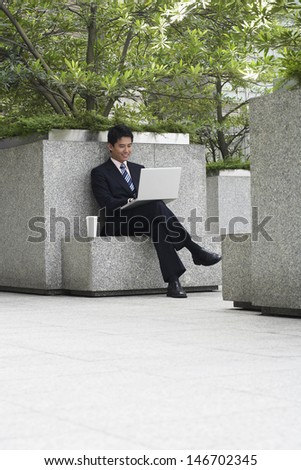 Full length of young businessman using laptop while sitting on stone bench