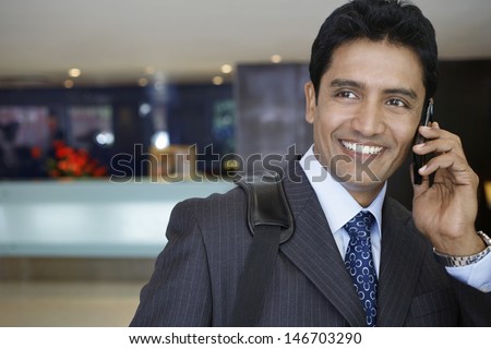 Closeup of confident young businessman using cell phone in hotel lobby