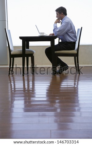 Full length side view of middle aged businessman using laptop at cafe