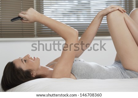 Side view of young woman in nightwear reading text message while lying on bed at home