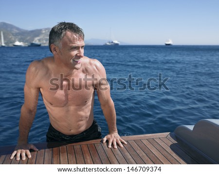 Middle aged man looking away while leaning on the edge of yacht\'s floorboard