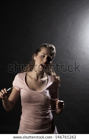 Happy teenage girl singing while listening music through MP3 player on gray background