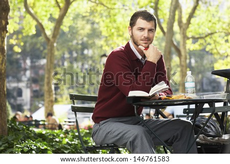 Portrait of confident young businessman holding book in park